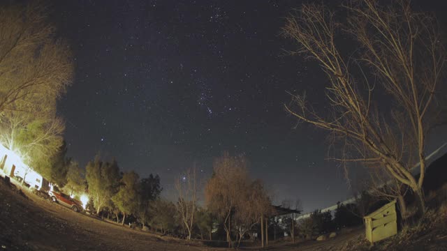 星星在沙漠的夜空中移动，前景是树和卡车，延时，鱼眼视频素材