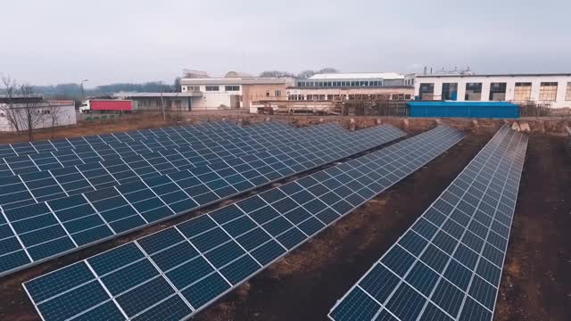 太阳能电池板农场在工业工厂的背景。飞越太阳能电池板场。可再生绿色替代能源概念。视频素材