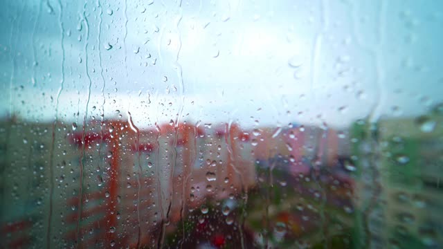 雨点落在城市的窗户上。下雨的天气，太阳在天空。在高层建筑的背景上，水滴在玻璃窗上流动。视频素材