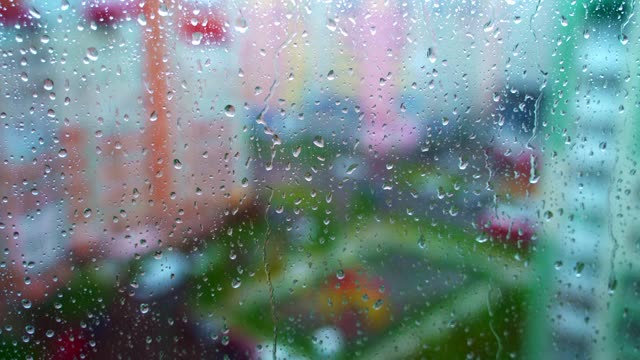 雨天的窗户模糊了城市背景。雨点打在窗玻璃上。抽象的雨滴风景背景。视频素材