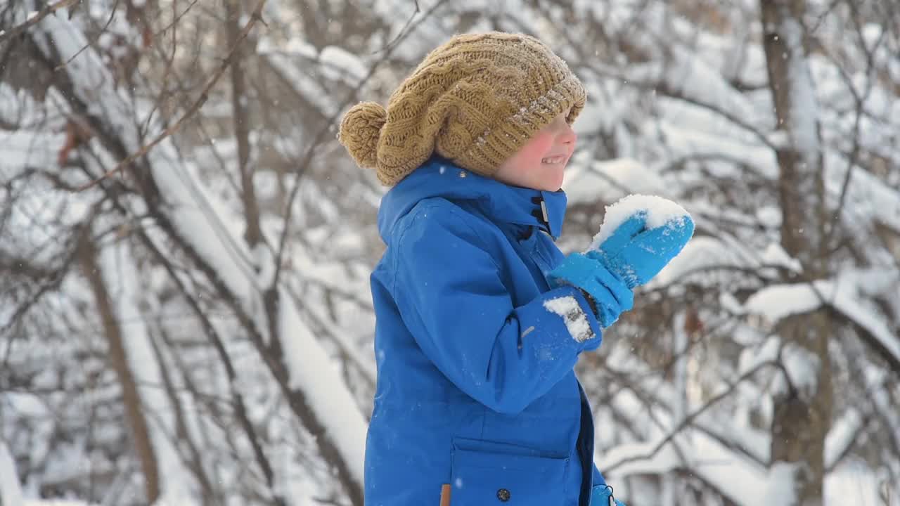 孩子吃新鲜的雪躺在他的手中。小男孩在玩新鲜的雪。在大雪纷飞的冬日，孩子们活跃的户外休闲活动。视频素材