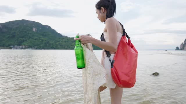 亚洲年轻女子收集塑料袋和玻璃瓶从海岸岛屿海滩旅行，捡垃圾志愿垃圾回收。生态环境意识视频素材