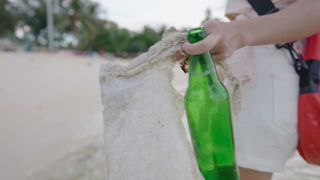 年轻女子走上海滩后，从海岸收集海洋垃圾，自然环境污染问题，志愿者清理海滩，全球变暖意识，从背后看视频素材