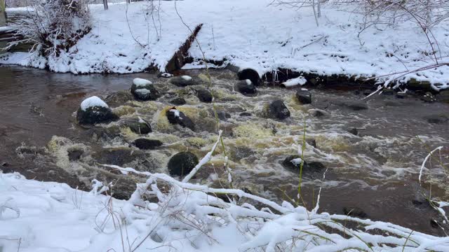 在冬天被雪覆盖的时候，在汹涌的河水上用小石头散步视频素材