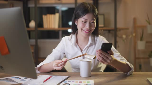 亚洲聪明的自由职业商业女性晚上在家里的客厅里用笔记本电脑工作的时候吃着方便面。股票视频素材