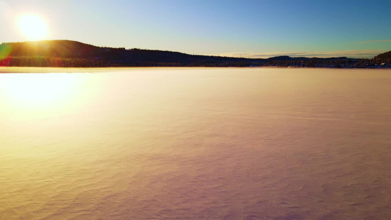 在日落时分飞过覆盖着闪闪发光的白雪的冰冻湖面。视频素材