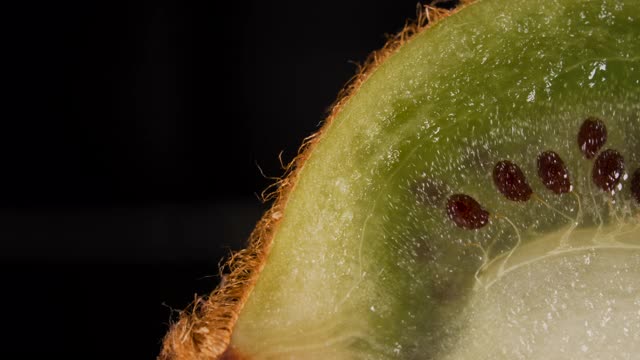 微距拍摄片新鲜的绿色猕猴桃和种子水果在黑色的背景。多汁新鲜成熟美味的切片猕猴桃，特写。视频素材