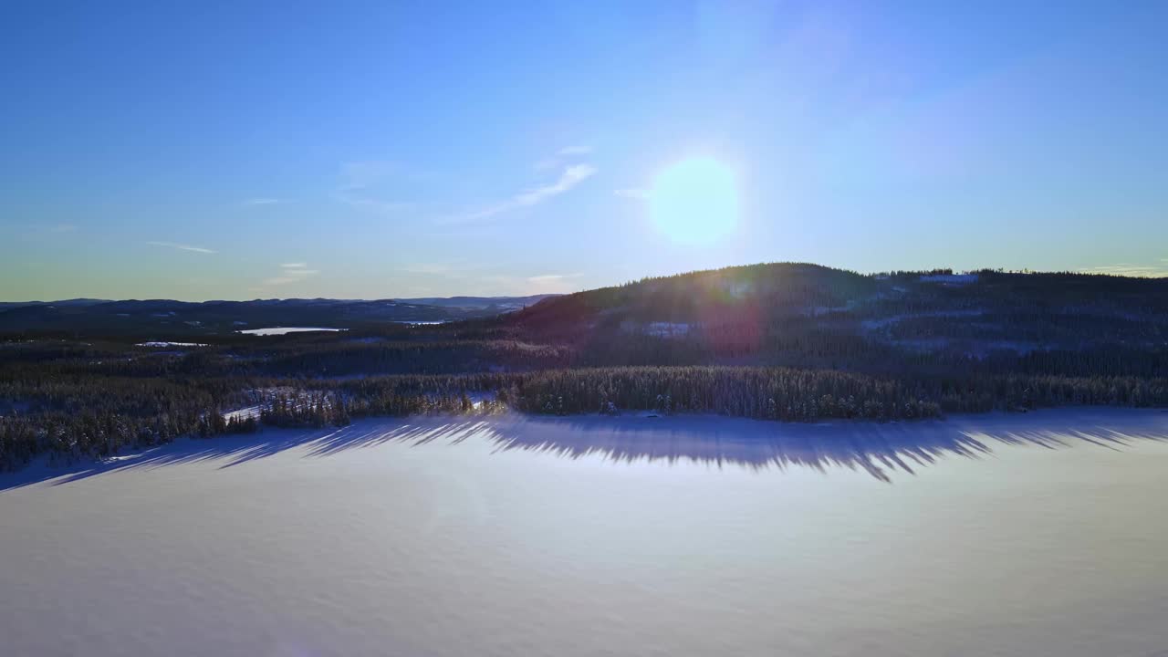 明亮的太阳落在北极的一个冰雪覆盖的树木和蓝色的天空的冬季仙境结冰的湖面上。视频素材