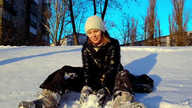 一个女人坐在雪地里，微笑着向镜头扔雪。视频素材