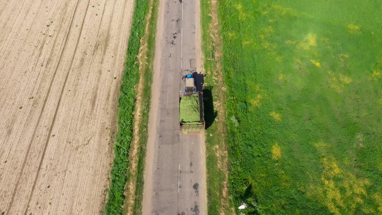 拖拉机与拖车满是割草收获的干草正在沿着乡村道路移动视频素材