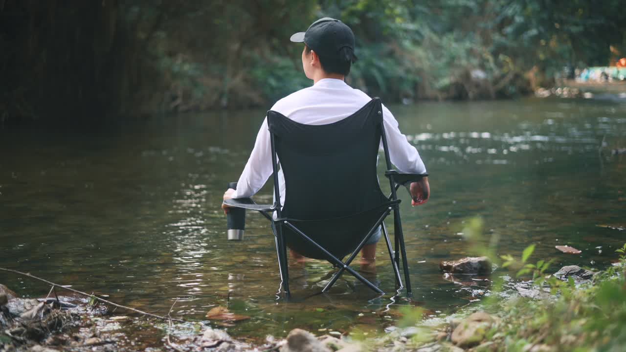 一个男人正坐在湖边，享受着大自然和咖啡，旅游放松的概念。视频素材