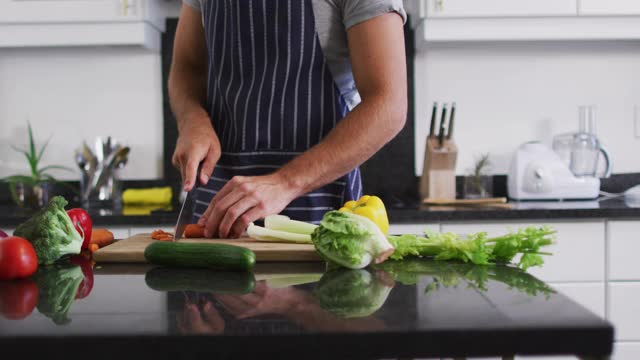 中部的白人男子穿着围裙在厨房里切菜视频素材