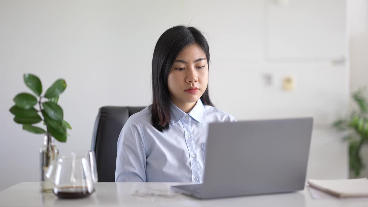 年轻美丽的亚洲商务女人的特写集中认真的女性与计算机工作。戴着时尚眼镜的专注商业女性坐在咖啡馆里用笔记本电脑工作。视频素材