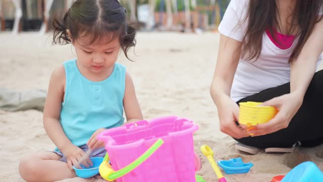 亚洲可爱的蹒跚学步的女孩喜欢和她的妈妈在沙滩上玩沙堡视频素材