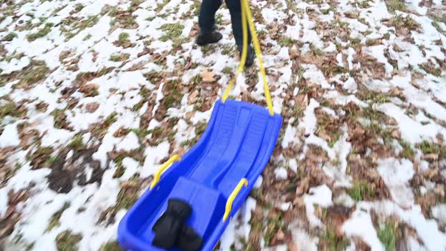 一个小孩拉着雪橇从草地上滑过，上面有一些雪。气候变化。视频素材