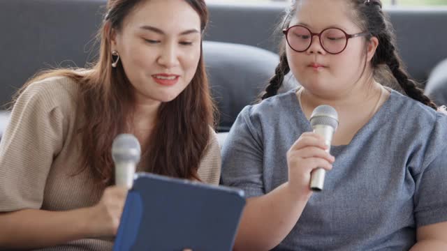 一个患有唐氏综合症的亚洲女孩和她的父母在客厅里唱歌视频素材