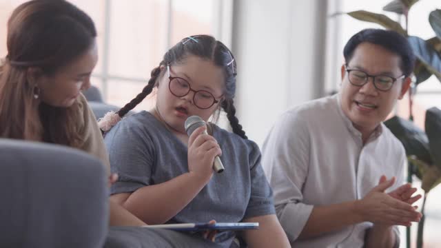 一个患有唐氏综合症的亚洲女孩和她的父母在客厅里唱歌视频素材