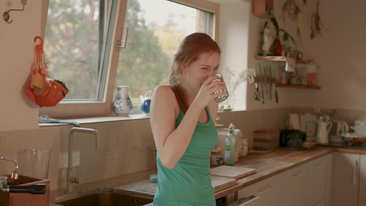 年轻女子在厨房里喝着一杯水视频素材