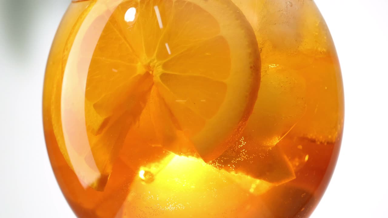 近距离的转变与冰块和水果片的橙aperol喷鸡尾酒杯视频素材