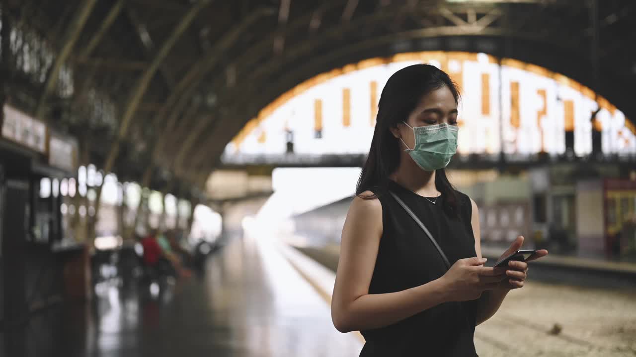 一名亚洲妇女在曼谷华兰蓬火车站等车，她要到空气污染严重的城市工作，戴着防护口罩，防止PM2.5、雾霾、空气污染视频素材