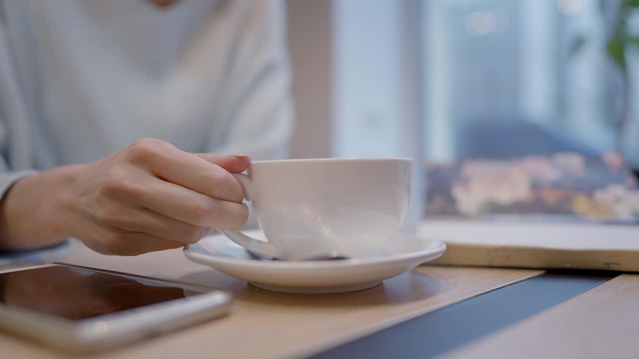 特写咖啡杯与女性的手拿热饮料。一个陌生的年轻白种女人在餐馆或咖啡馆休息。休闲和生活方式的概念。视频素材