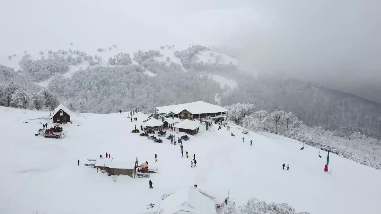 度假的人们聚集在山顶上，用滑雪板或滑雪板往下滑。一个可以让你暖和起来，喝热饮的房子。视频素材