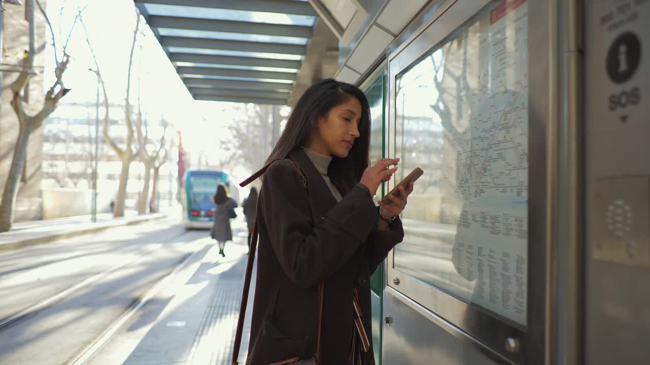 一个女人拿着智能手机在电车站看地图视频素材