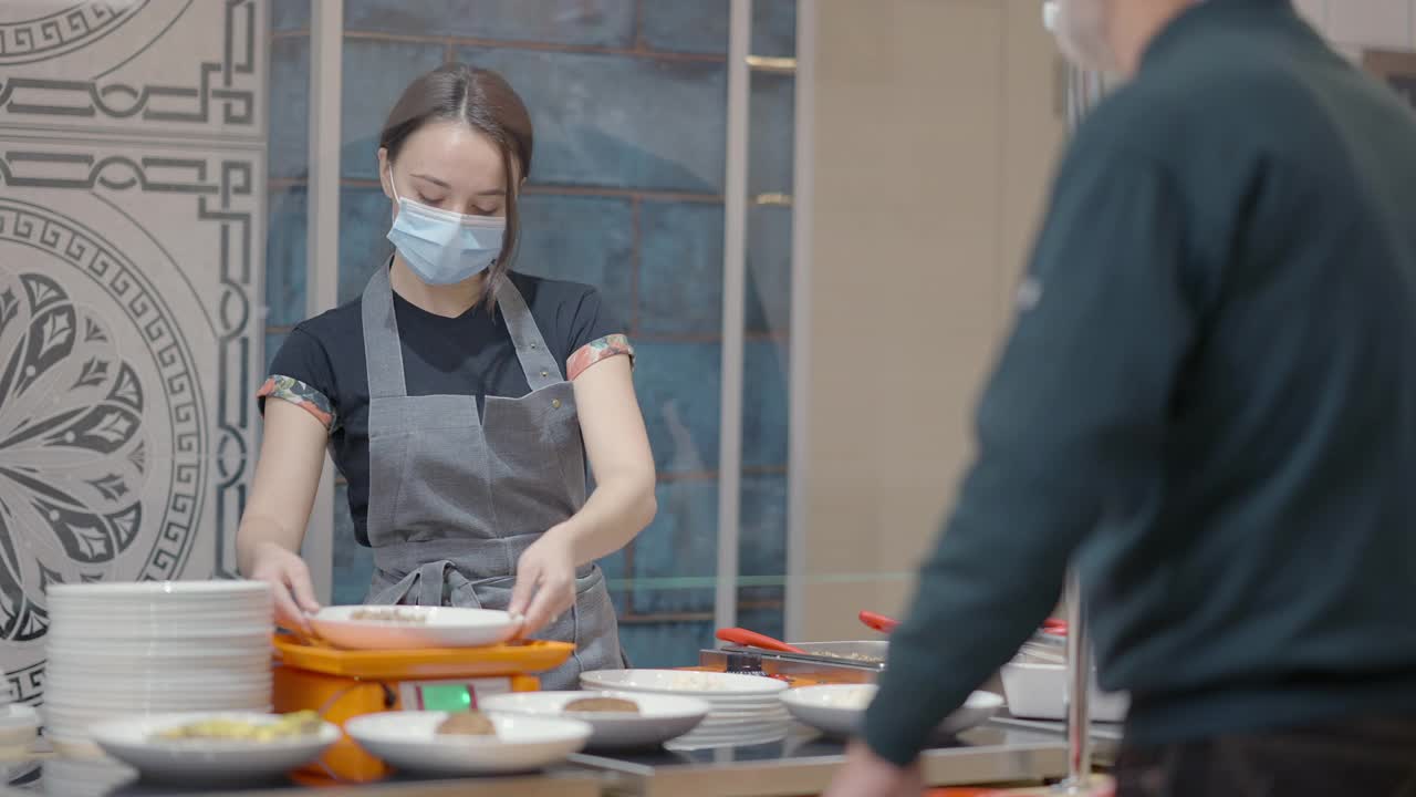 苗条的年轻女服务员在自助餐厅称量食物，并为资深男性客户提供午餐。戴着新冠肺炎口罩的白人妇女在餐厅为退休男性服务。视频素材