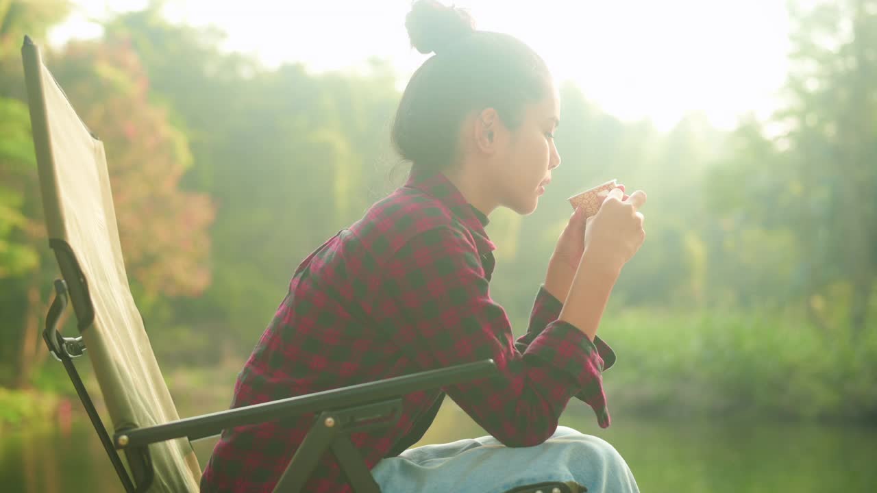 一个美丽的年轻旅行者女人是享受与自然喝咖啡在早晨湖，放松，露营假日和旅游概念。视频素材