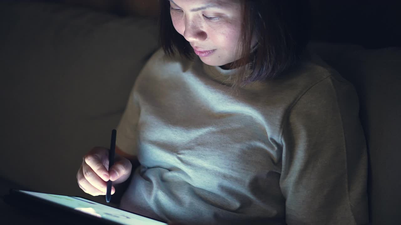 女人使用数码铅笔和数码平板电脑在晚上的时间在家里视频素材