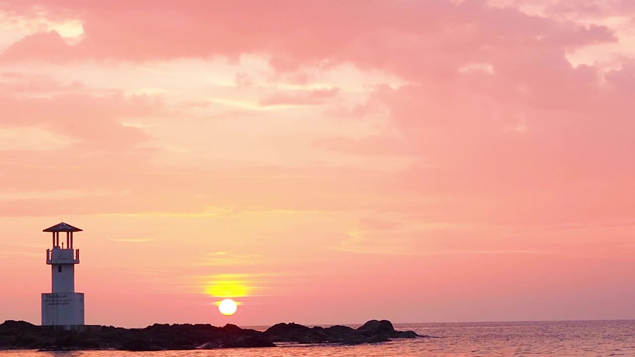 柔和的橘红色天空在日落的海边与美丽宁静的小灯塔矗立着坚定的风景。浪漫的景观背景，b卷抽象多彩的自然云景镜头。视频素材