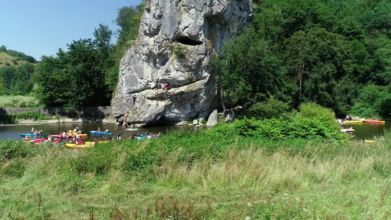 夏季活动鸟瞰图。人们从高悬崖跳进水里，一群皮划艇手划下来。绿色景色，岩石峡谷景观。在炎热的夏天划皮划艇和游泳视频素材