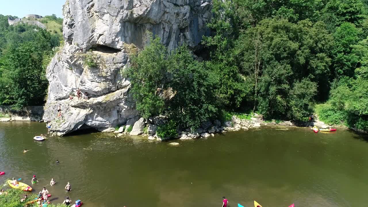 夏季活动鸟瞰图。人们从高悬崖跳进水里，一群皮划艇手划下来。绿色景色，岩石峡谷景观。在炎热的夏天划皮划艇和游泳视频素材