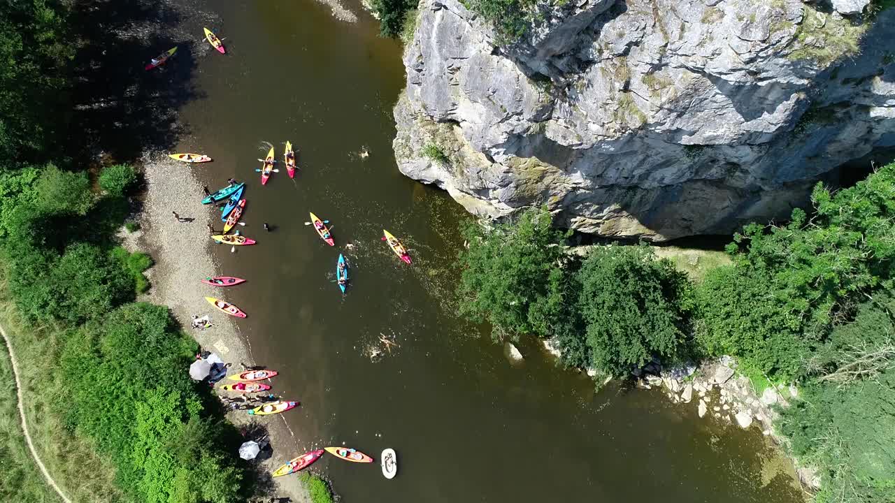 夏季活动鸟瞰图。人们从高高的岩石/悬崖跳进水里，一群皮划艇手划下来。绿色景色，岩石峡谷景观。在炎热的夏天划皮划艇和游泳视频素材