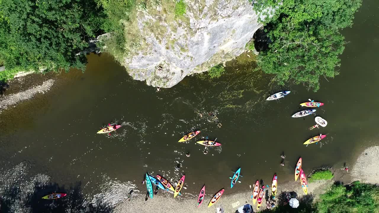 夏季活动鸟瞰图。人们从高高的岩石/悬崖跳进水里，一群皮划艇手划下来。绿色景色，岩石峡谷景观。在炎热的夏天划皮划艇和游泳视频素材