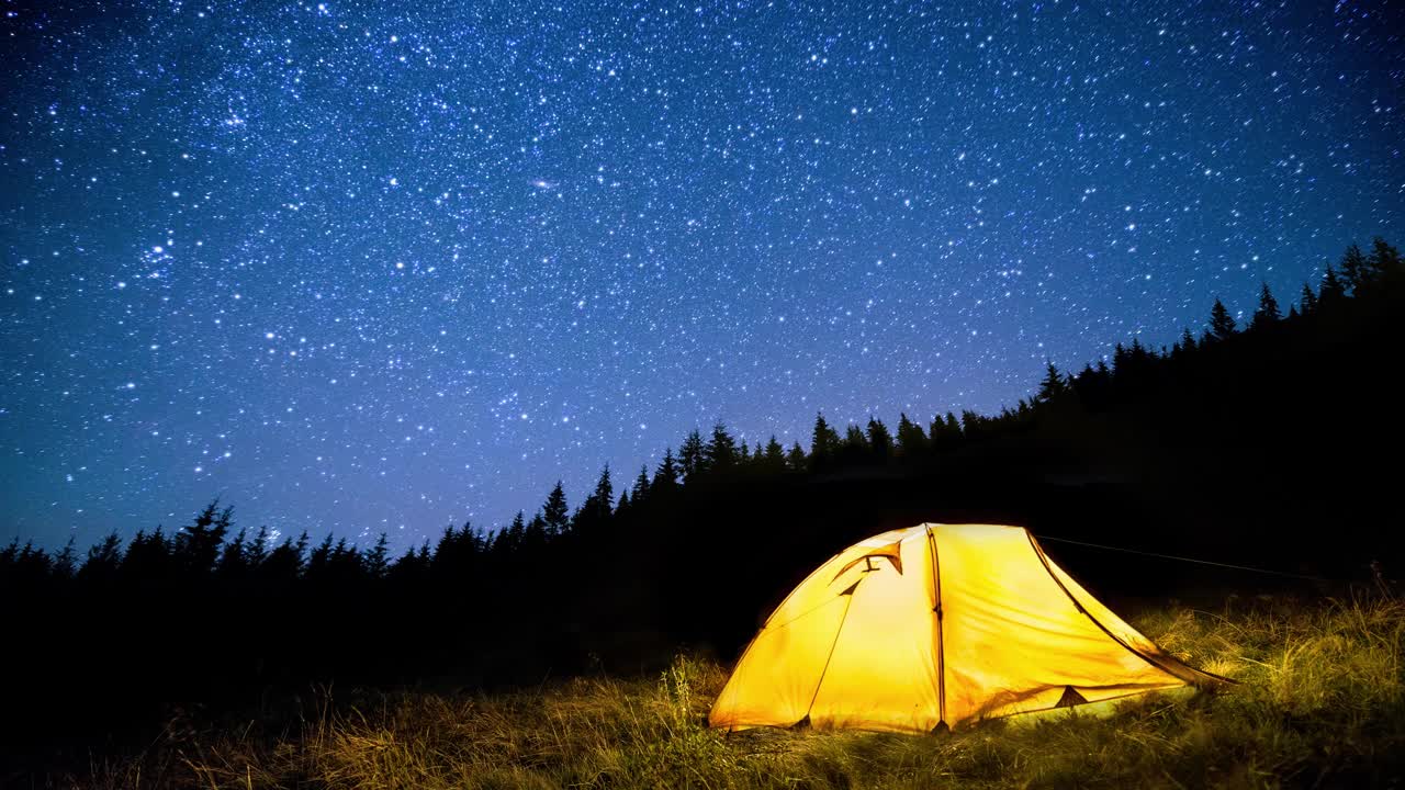 在闪烁的星空下，夜深人静的山林中闪闪发光的露营帐篷。Cinemagraph。视频素材