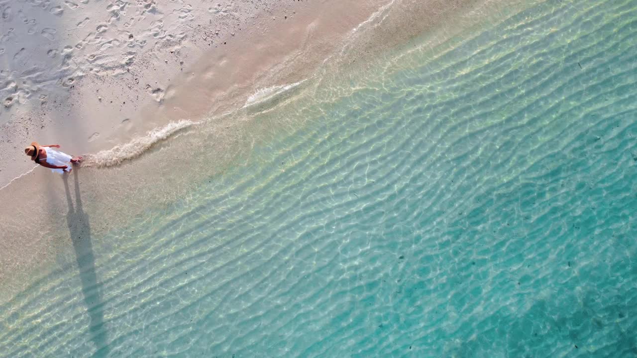 年轻女子坐在和放松在美丽的热带白色沙滩海浪泡沫和透明的海，暑假和旅行背景从无人机俯视视频素材