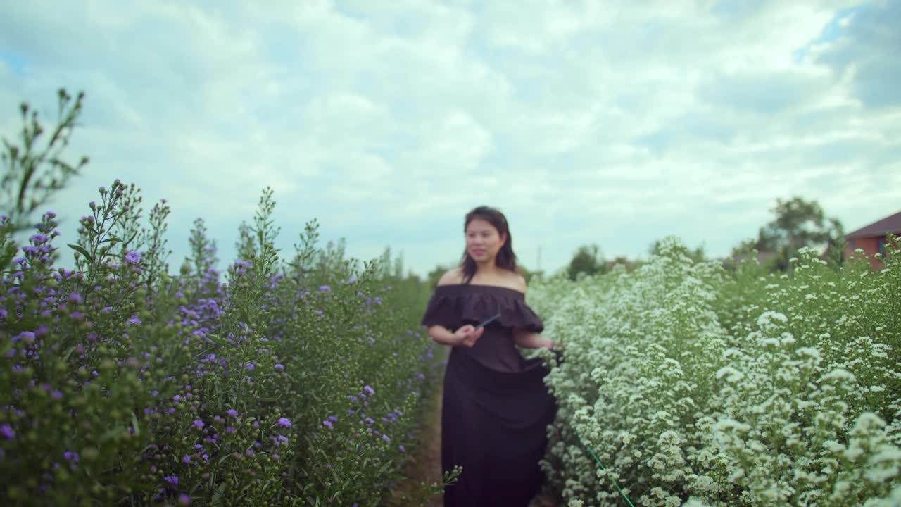 年轻迷人的亚洲女性穿着休闲服装沿着白色绿色美丽的花朵自然农场独自漫游的旅游理念走着，带着积极的情绪移动身体视频素材