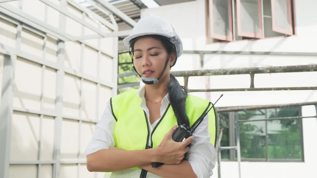 亚洲女工的肖像，人们戴着防护安全帽和眼镜现场的建筑。女工程师站在那里，交叉着胳膊，微笑着看着镜头。视频素材