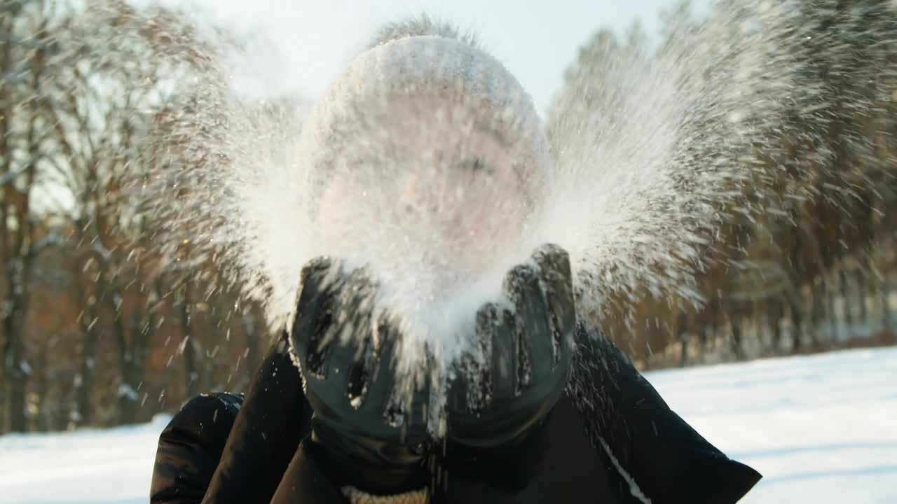 在一个阳光明媚的冬日，漂亮女人从她的手掌上吹雪。视频素材