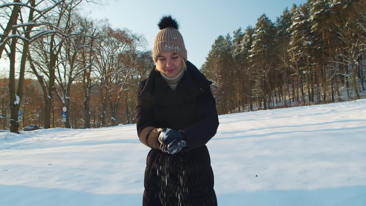 开朗漂亮的金发女郎穿着冬装，开心地玩雪球，把它们扔向朋友。视频素材