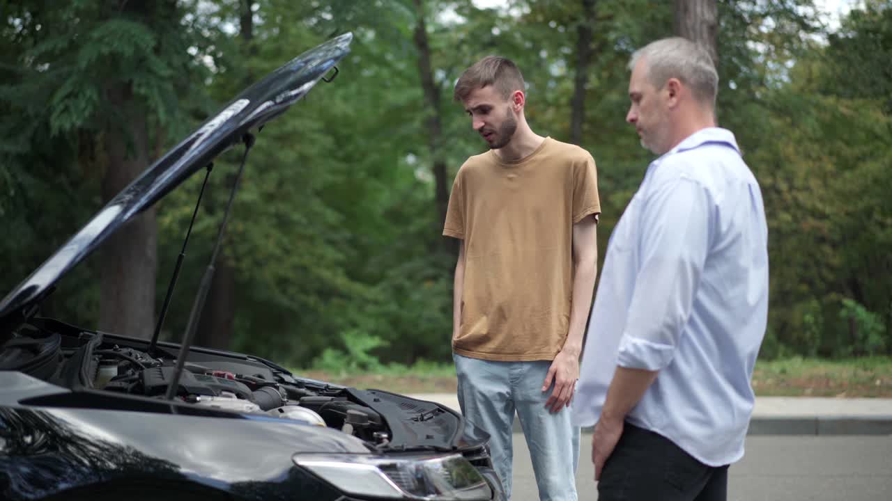 肖像沮丧的年轻白人男子还车钥匙惹恼父亲站在破车在夏天的道路上。强调不负责任的儿子弄坏了汽车。视频素材