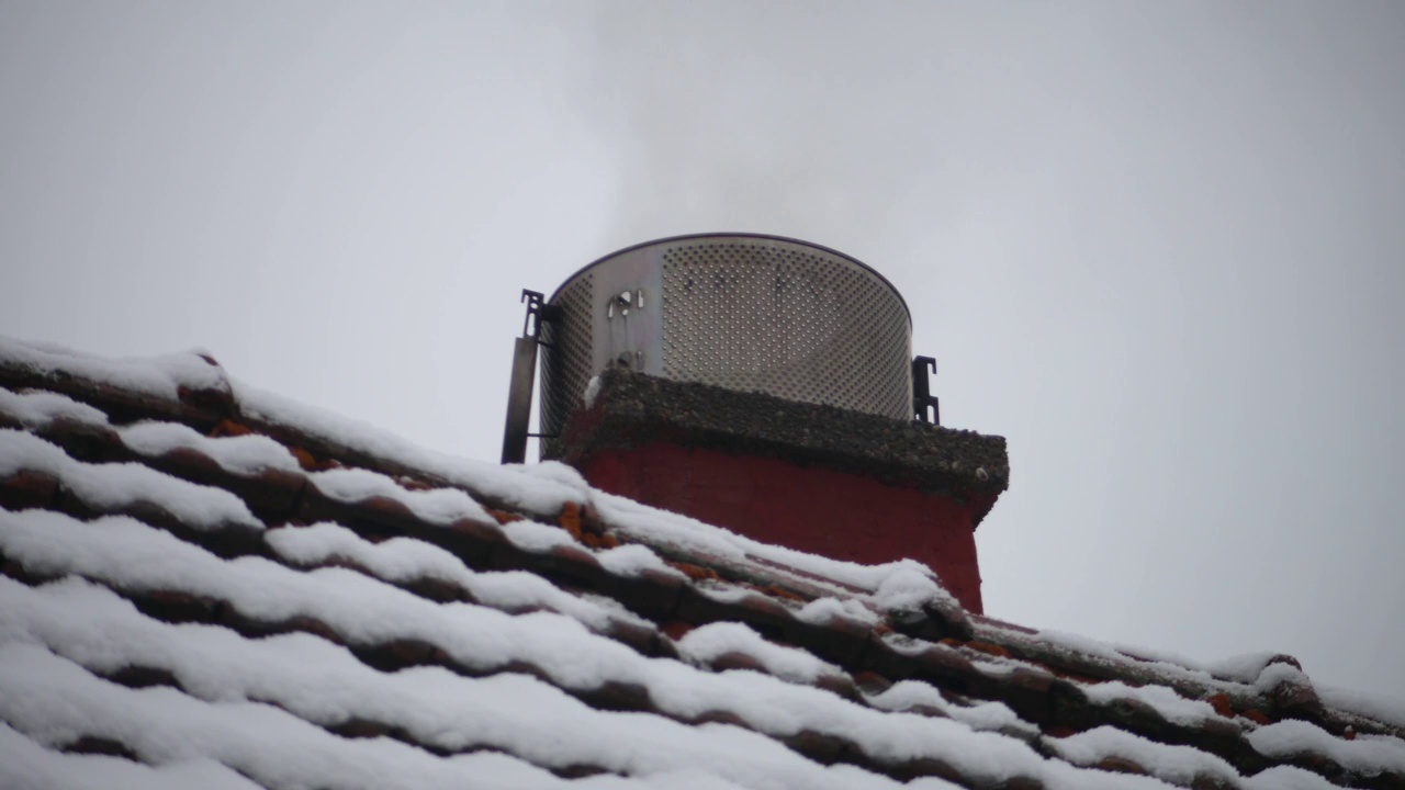 灰色的烟雾从烟囱和屋顶下的雪视频素材