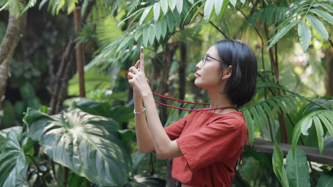 年轻的亚洲女子在花园里用手机拍照视频素材