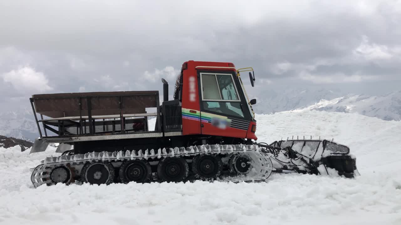 在滑雪场，一辆红色的4K雪车在白天清理积雪。在白雪皑皑的群山映衬下视频素材