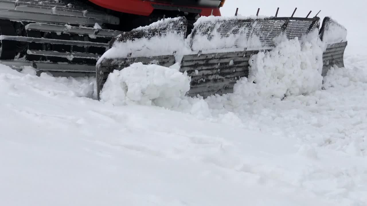 近距离的工作，宽雪车骑在雪和耙它的背景雪山。为滑雪季节和采雪准备雪坡的概念视频素材