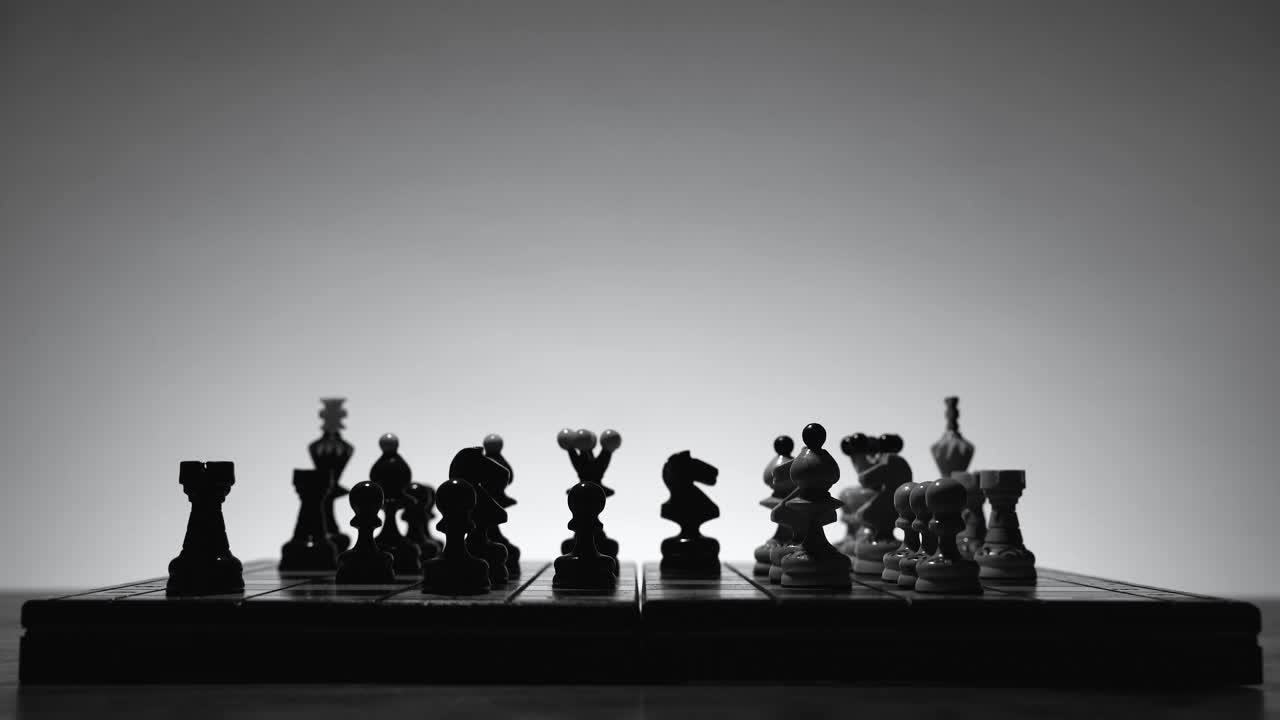 国际象棋的游戏。棋盘与棋子的剪影在白色的背景。商业理念、竞争和战略理念的概念。黑白经典艺术照片。视频素材