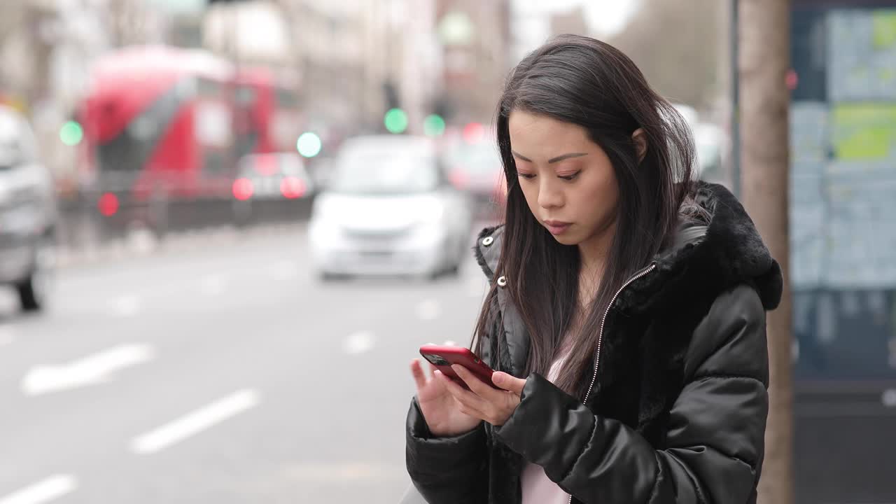 一名中国女子在公交车站等车，她在用智能手机视频素材