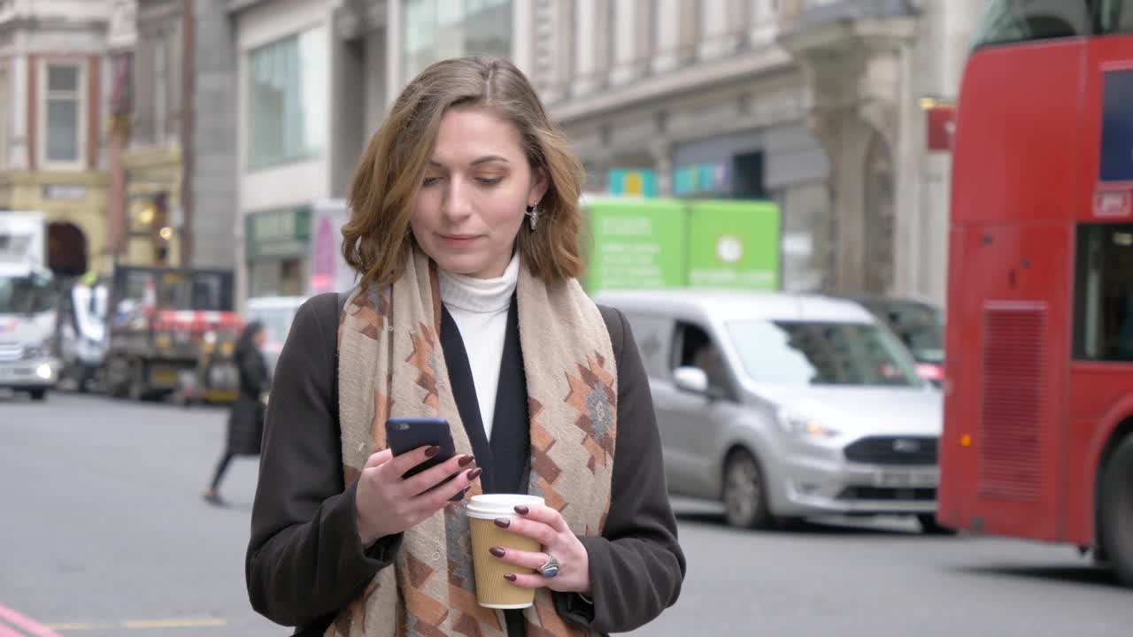 在伦敦，一个金发女人一边拿着咖啡杯一边用手机大笑视频素材