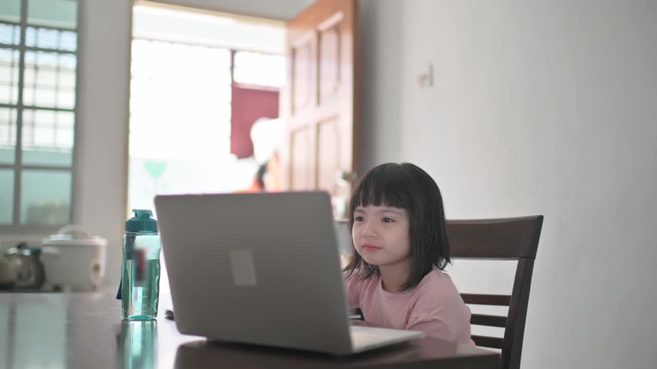 亚裔中国女孩在她姐姐的帮助下在厨房餐桌上参加网络课程视频素材